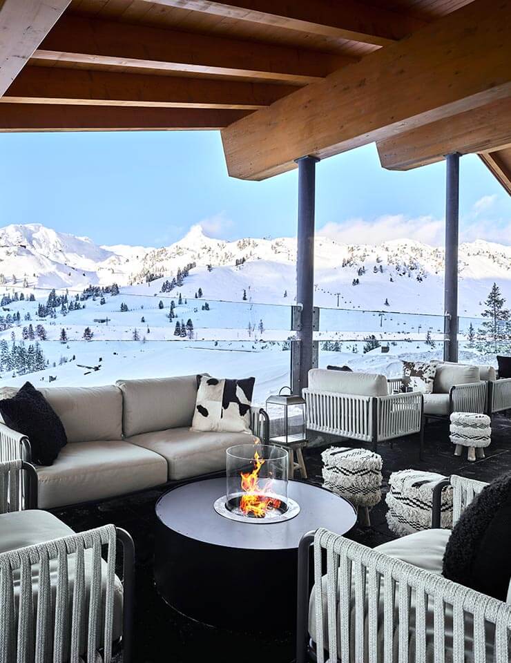 Terrace view of the rooftop bar at OBERTAUERN [PLACESHOTEL] showcasing stunning snowy mountain peaks in the background.